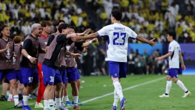Soccer players celebrate on the field, arms outstretched to greet a teammate wearing number 23 with 'HUMMET' on the back.