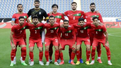 Iran national football team posing for a group photo on the pitch in red uniforms with green accents.
