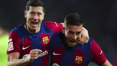 Two Barcelona players celebrate together on the pitch, arms around each other, wearing blue and red striped jerseys with the club crest visible.