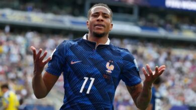 French national team footballer in a blue kit with number 11 celebrates with arms raised on the pitch.