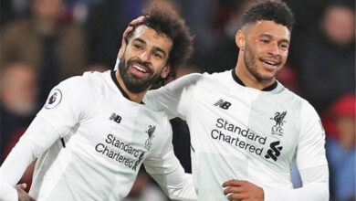 Two Liverpool football players in white kits celebrate together on the pitch with arms around each other.